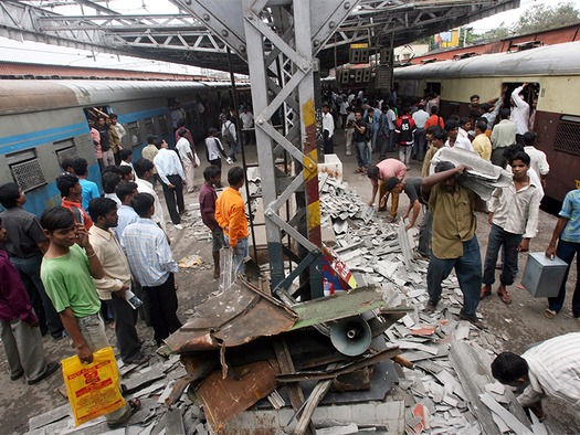 WEB Workers clear debris from railway station platform damaged by bomb explosion as commuters waiting for their train watch in Mumbai