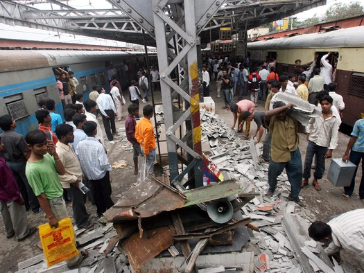 PRINT Workers clear debris from railway station platform damaged by bomb explosion as commuters waiting for their train watch in Mumbai